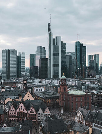 xuits-Stadtansicht mit Fachwerkhäusern, großem Gebäude mit grünem Dach, Wolkenkratzern und bewölktem Himmel.