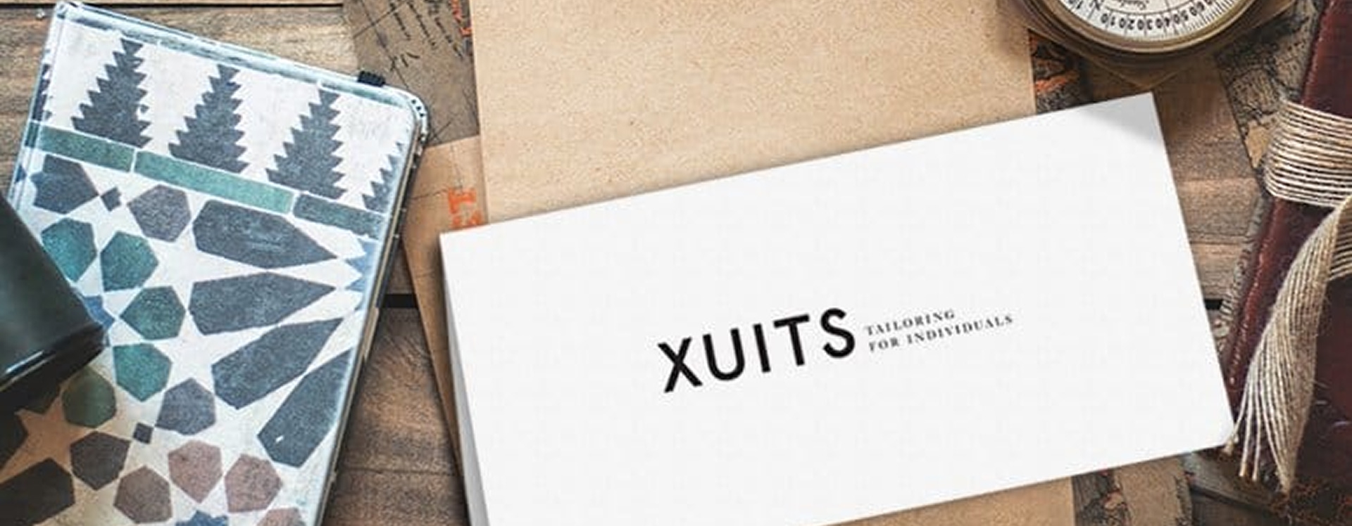 xuits -Weiße Visitenkarte mit XUITS Logo und Slogan, umgeben von braunen Umschlägen und gemustertem Stoff.