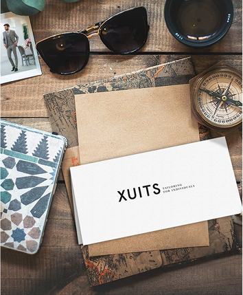 xuits-Holztisch mit Sonnenbrille, Kompass, Tasse, Postkarte, Musterheft und XUITS Briefumschlag.