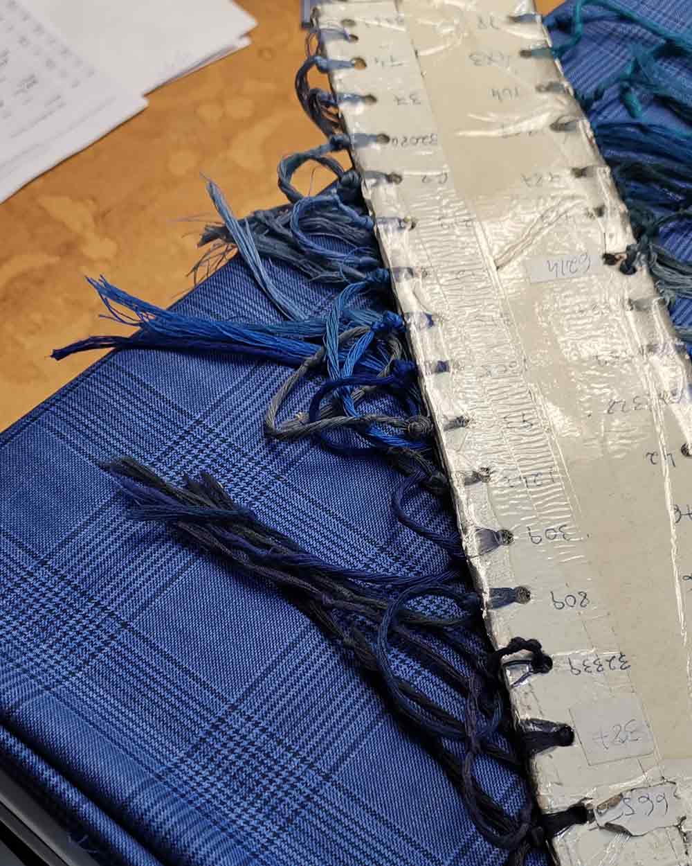xuits-Blaue Stoffmuster mit Fransen liegen auf Holztisch neben Kunststoffstreifen mit Notizen.