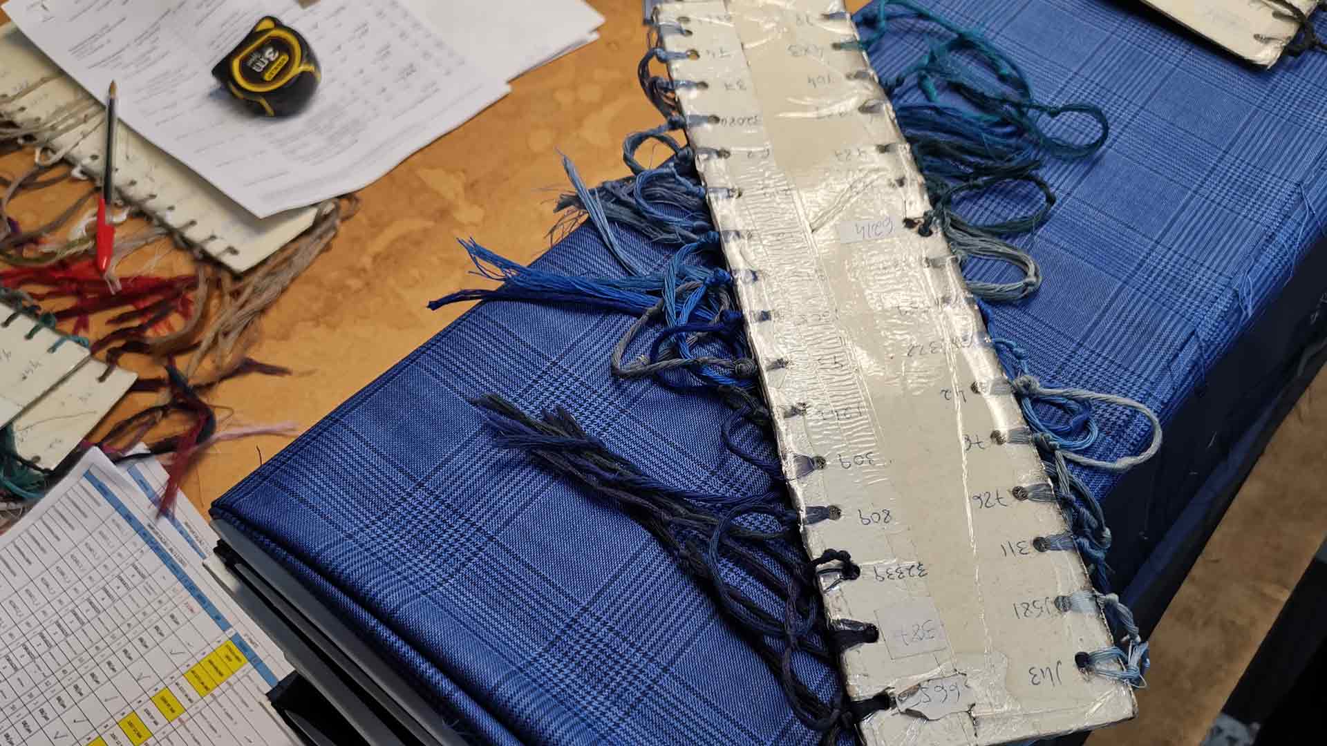 xuits -Musterbücher mit blauen Stoffmustern, Garnproben, handschriftlichen Notizen, Maßband und Bleistift auf Tisch.