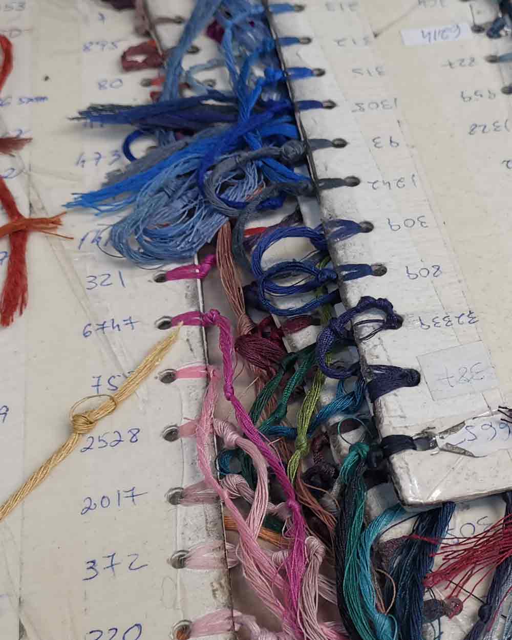 xuits -Sammelmappen mit bunten Garnfäden in Blau-, Rosa-, Grün- und Rottönen und handschriftlichen Zahlen.