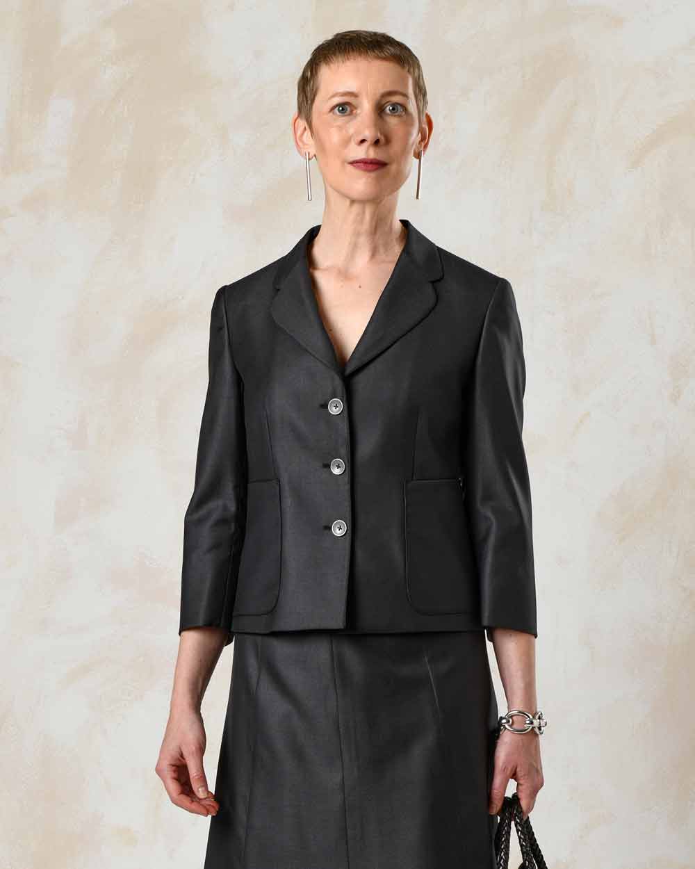 xuits-Frau mit kurzem Haar trägt schwarzen Blazer mit drei Knöpfen, passendem Rock und silbernem Armband.
