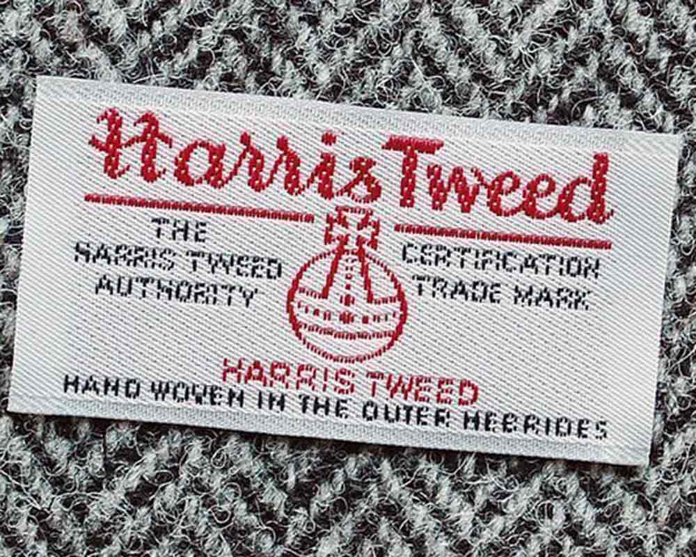 xuits -Stoffetikett Harris Tweed mit Harris Tweed Authority und Handgewebe-Hinweis auf grauem Stoff.