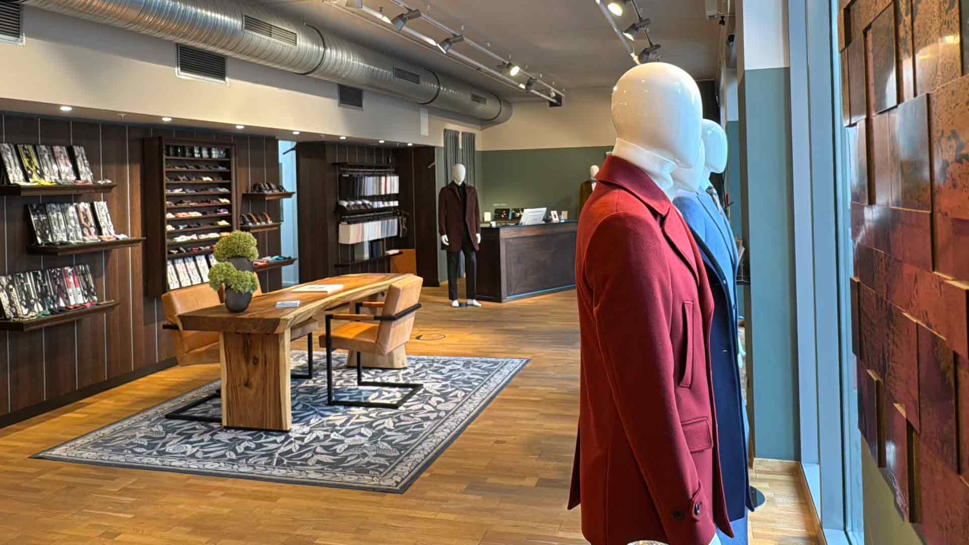 xuits -Modern eingerichteter Herrenausstatter mit Mänteln an Schaufensterpuppen, Holztisch und Regalen.