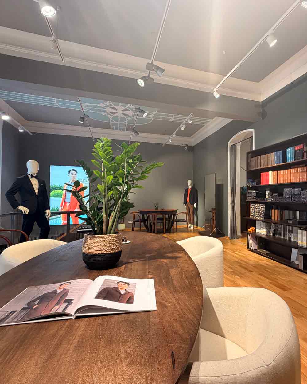 xuits -Moderner Showroom mit Holztisch, weißen Stühlen, Schaufensterpuppen und Bücherregal.