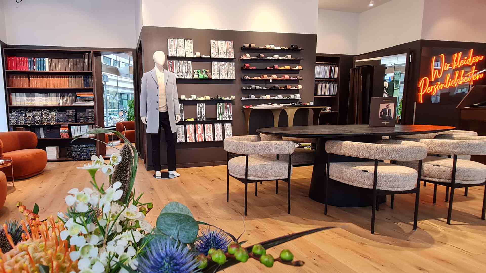 xuits -Verkaufsraum mit Holztisch, gepolsterten Stühlen, Schaufensterpuppe, Accessoires und Neon-Schild.