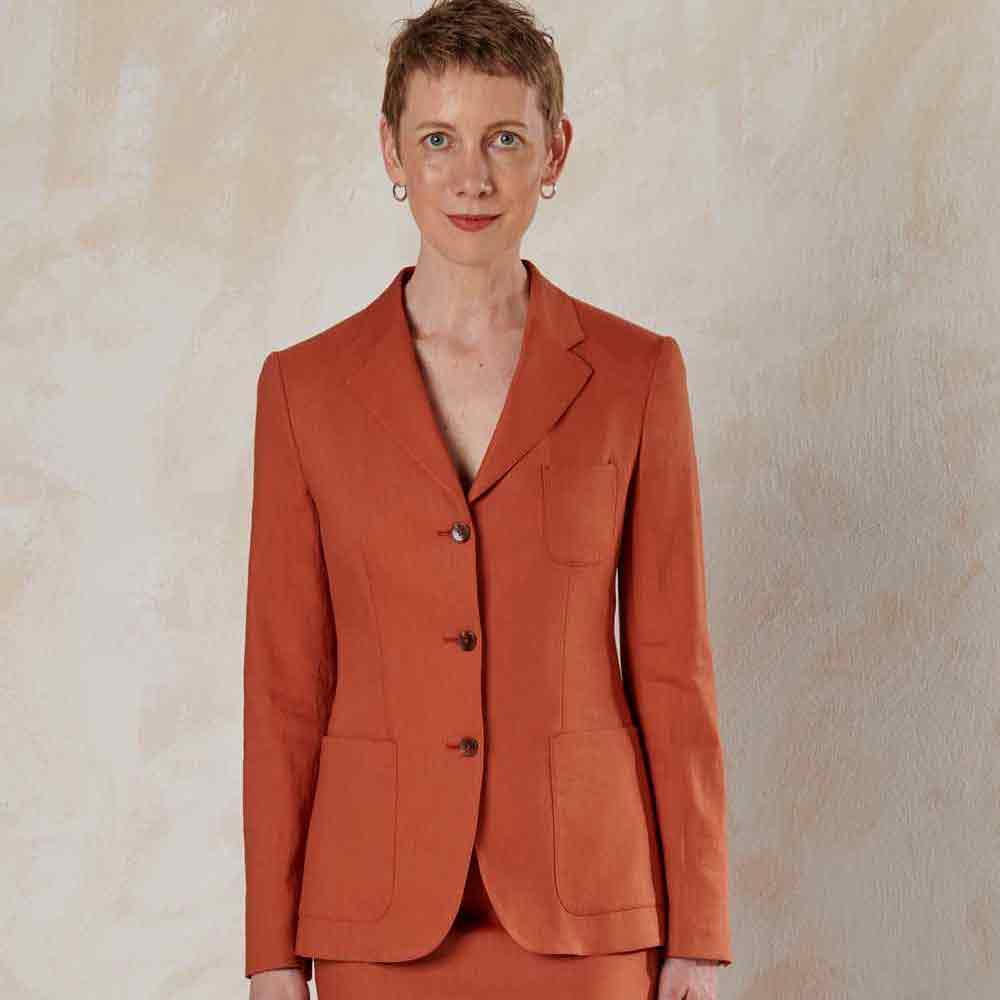 xuits-Frau mit kurzem Haar trägt orangerotes Blazer-Kostüm vor hellem strukturiertem Hintergrund
